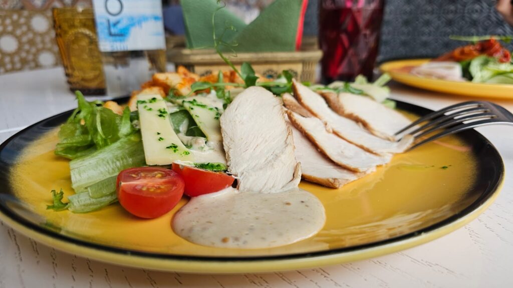 Ensalada César con pollo, queso parmesano, lechuga, croutones y aderezo en un plato elegante